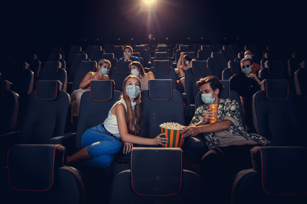 Cinéma, salle de cinéma pendant la quarantaine. Règles de sécurité en cas de pandémie de coronavirus, distance sociale pendant la séance de cinéma. Des hommes et des femmes portant un masque de protection sont assis dans les rangées de l'auditorium et mangent du pop-corn.