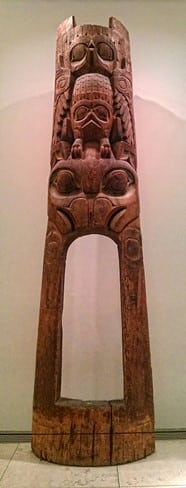 Wooden carved totemic doorway, with traces of red and blue colouring, representing an eagle / Wikicommons.